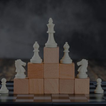 White chess pieces arranged on stacked wooden blocks in a pyramid formation, symbolizing strategic partnership and leadership structure.
